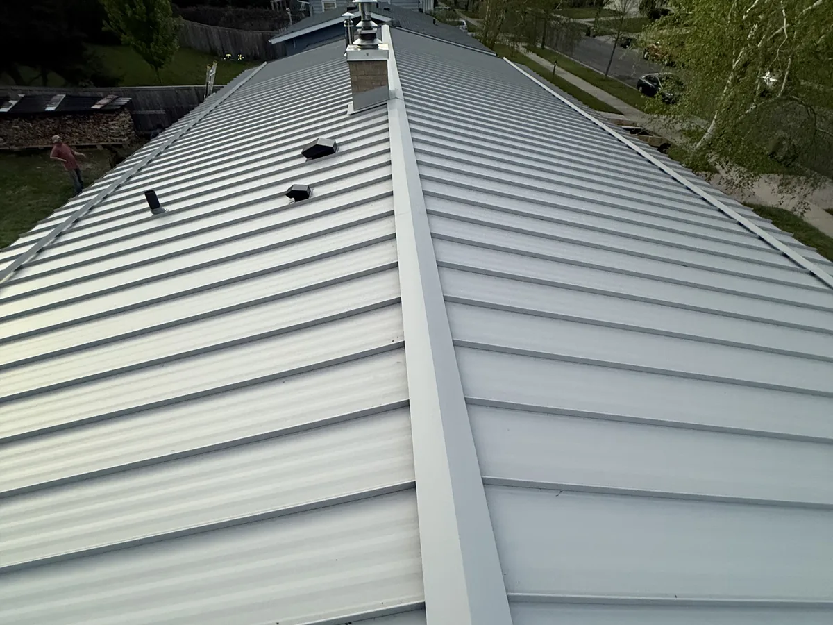 Silver standing seam metal roof beside a chimney